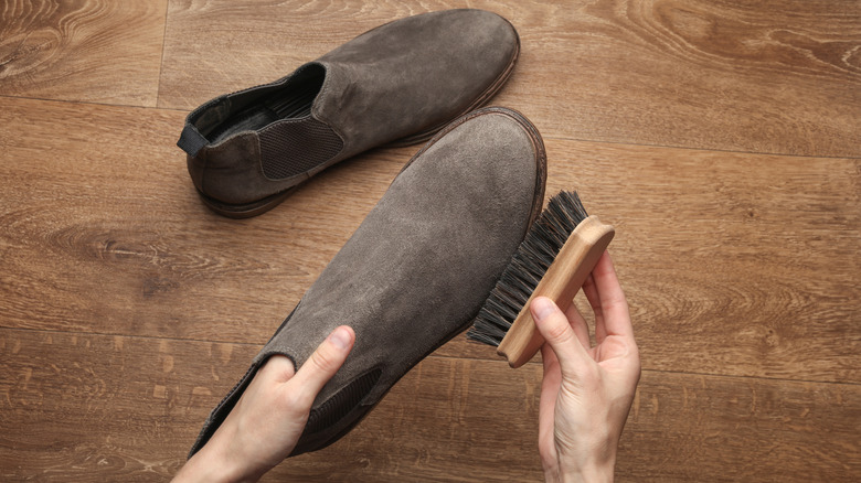 Hands cleaning suede boots using a bristled shoe brush