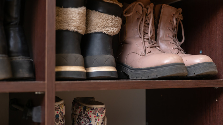 Winter boots sit in a wooden shoe organizer inside a closet