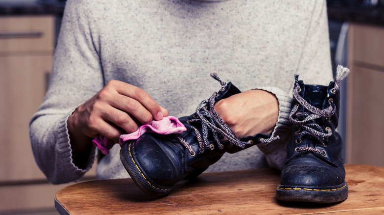 Man sits at a table polishing his boots with a pink microfiber towel