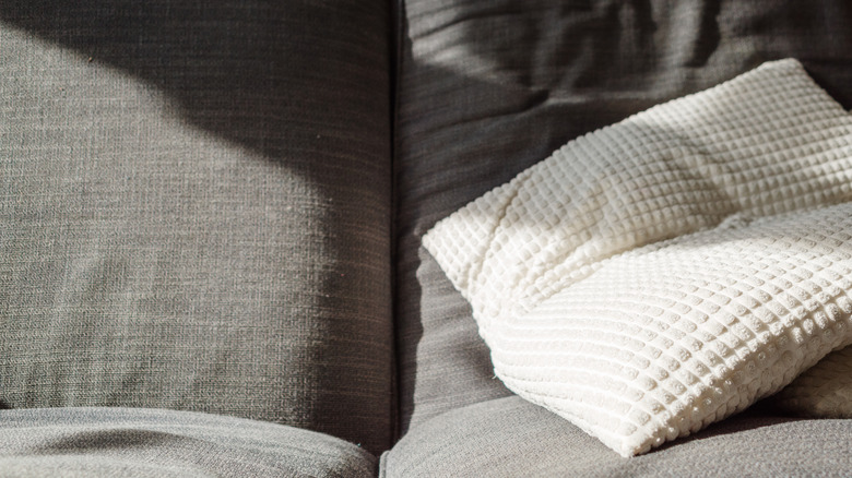 A gray sofa with a flat throw pillow.