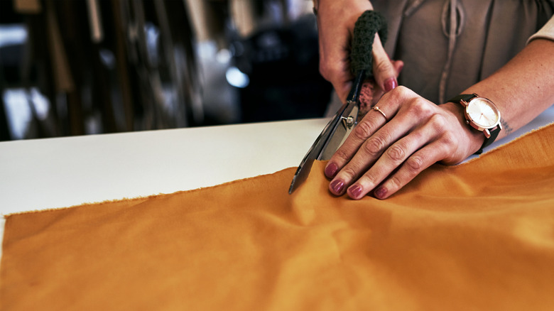 A woman cuts some orange material with fabric scissors.
