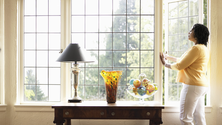 A woman opens a window in a set of windows with no curtains.