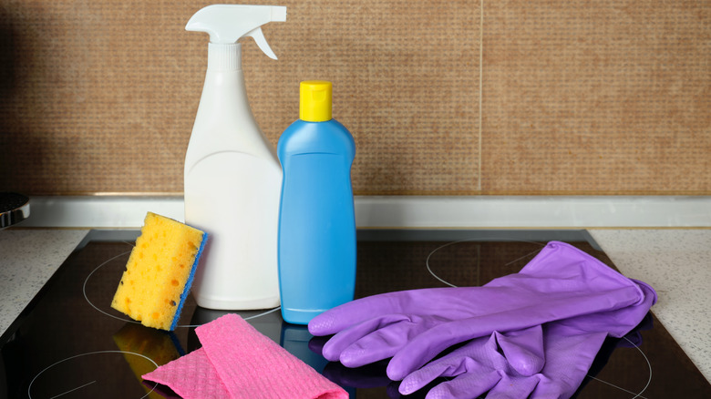 Cleaning products, including a spray bottle, a sponge, and a pair of purple gloves on an oven top