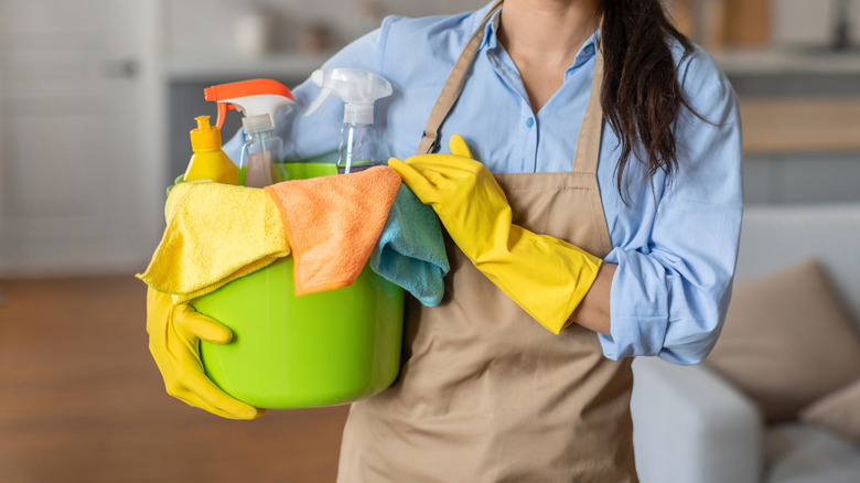 Someone holding a bucket-full of cleaning supplies and wearing an apron and yellow gloves