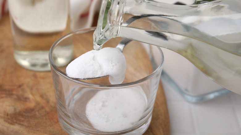 Someone pouring vinegar over baking soda in a glass