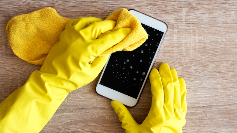 Gloved hands wiping cell phone