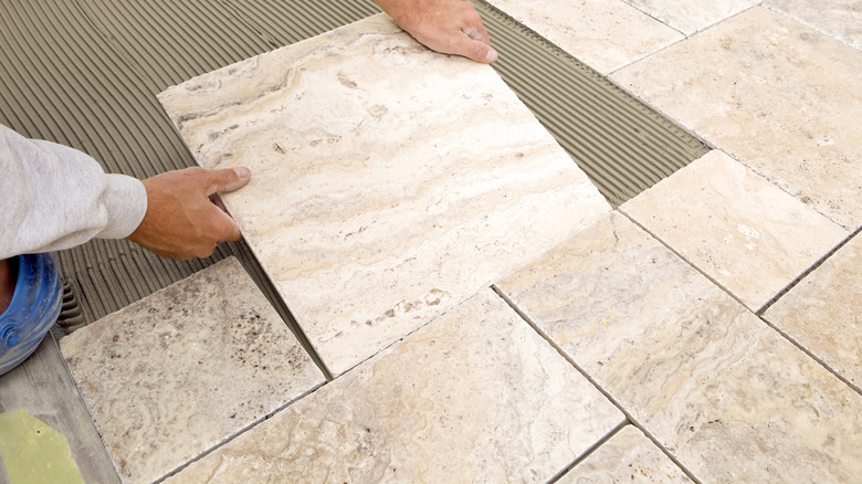 A person installs natural stone tile flooring