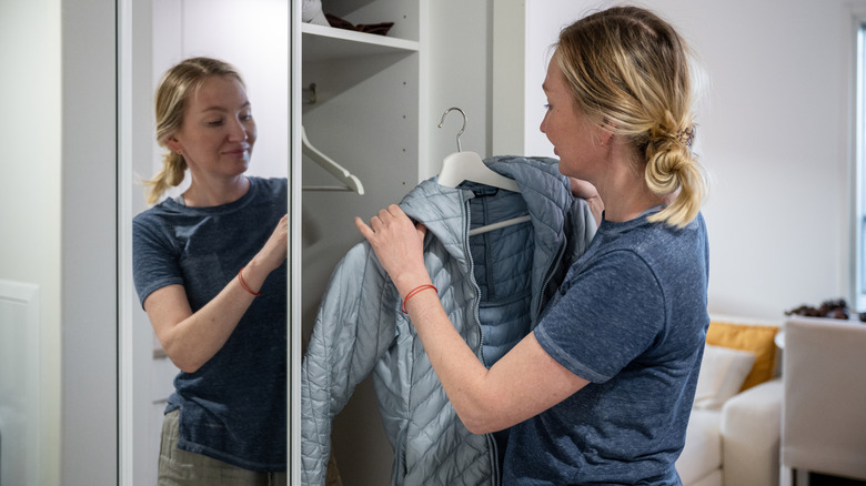 Woman hanging up blue jacket in closet