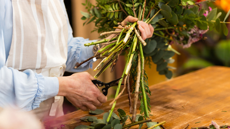Person's hands holding a bouquet while cutting its ends with floral scissors