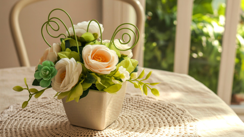 A short, square vase on a table holding a beautiful arrangement of pink roses.