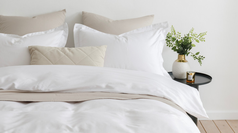 A white and beige bed made with the duvet folded down in front and pillows leaning against the wall.