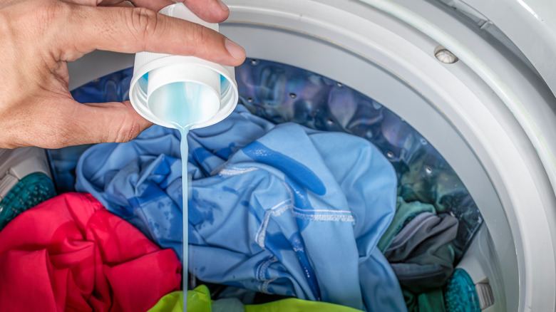 A person pours laundry detergent into a washing machine filled with laundry.