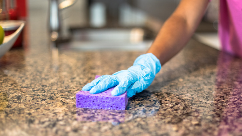 A person cleans a stone countertop with a sponge.