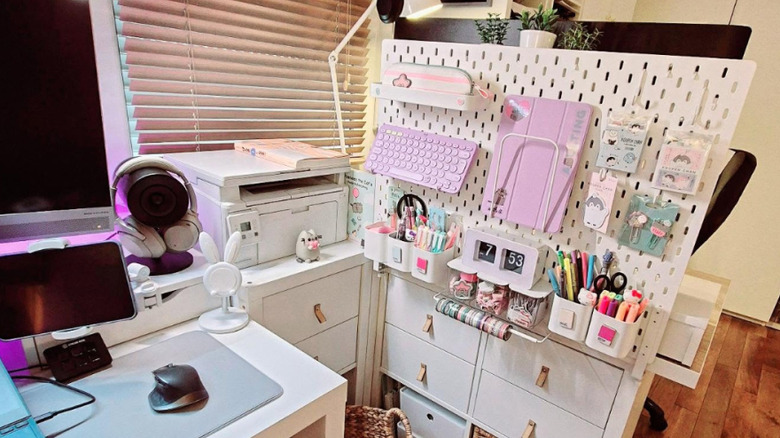 A white IKEA pegboard in the space between two home offices, displaying pens, a computer keyboard, and  other accessories