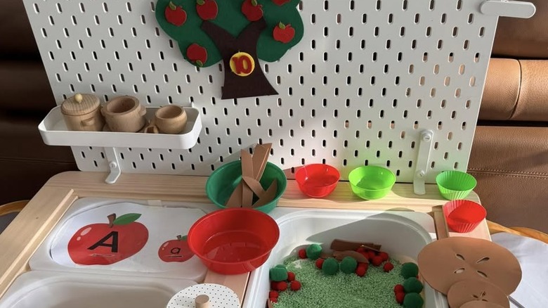 An IKEA pegboard is attached to a FLISAT table, and both hold supplies for children's sensory play