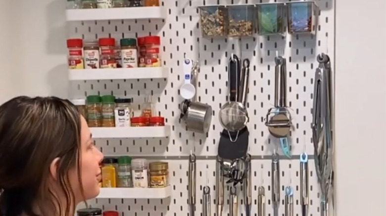 Spice jars and other kitchen supplies are attached to an IKEA pegboard mounted to a wall