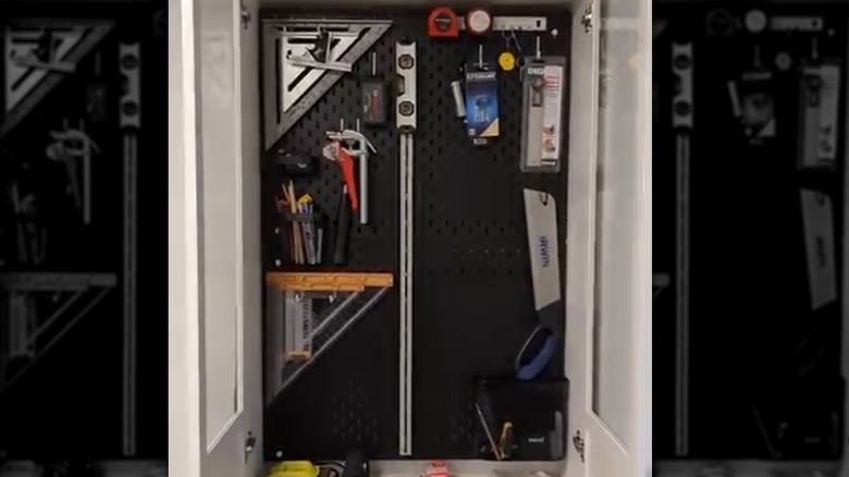 An IKEA pegboard inside a white bookcase holds tools, visible behind a glass panel